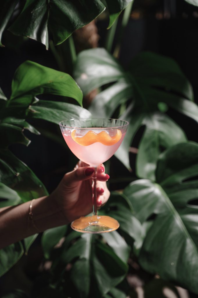 Pink cocktail held among tropical leaves